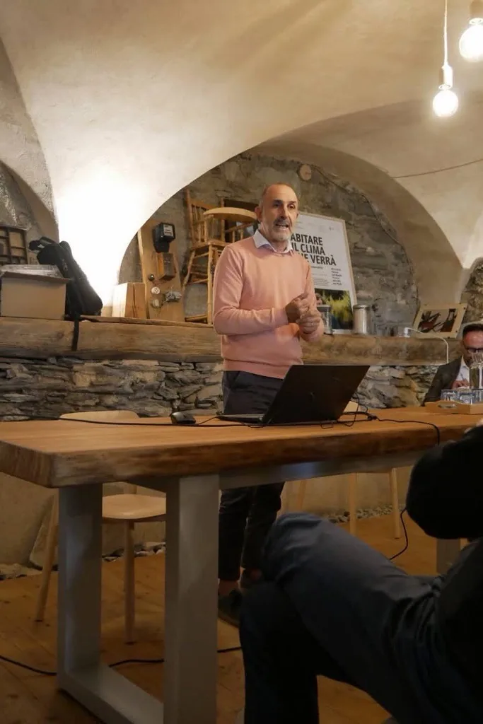 Elvio Rostagno in piedi mentre parla durante un incontro, in una sala con volte in pietra.