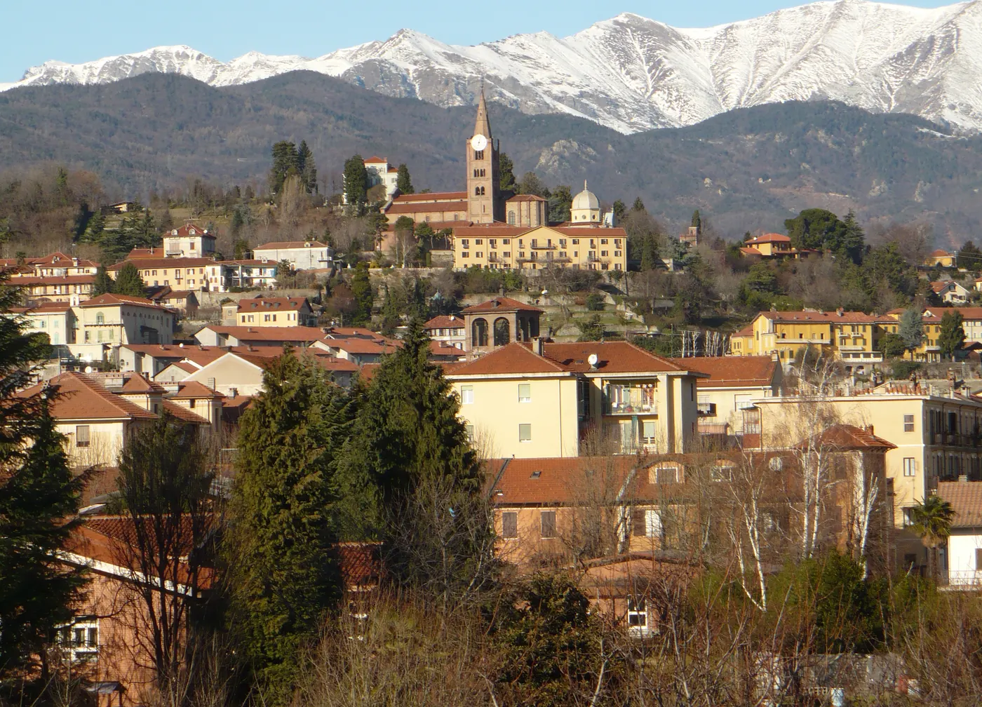 Pinerolo vista dalla città bassa: le case, la collina con la chiesa di San Maurizio e, dietro, le montagne innevate delle valli.